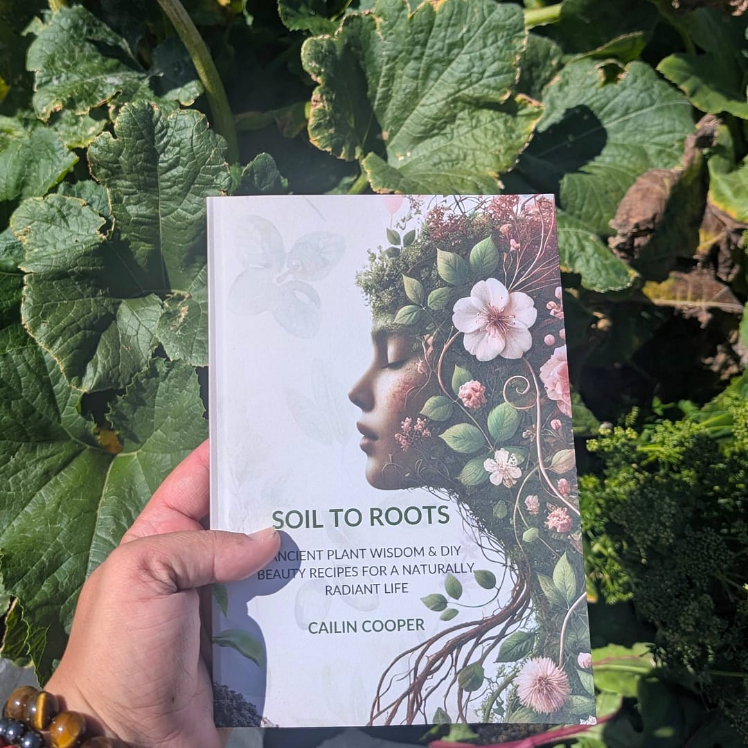 Soil to Roots Ancient Plant Wisdom & DIY Beauty Rituals 1 Soil to Roots book held in garden surrounded by green plants natural beauty guide
